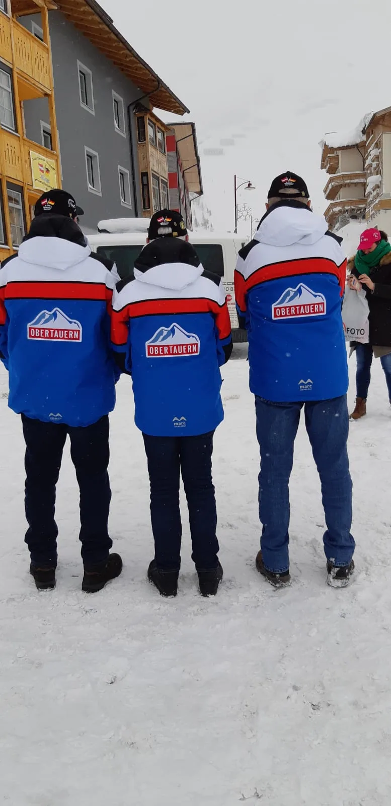Drei Personen von hinten in Jacken mit Logo auf dem Rücken