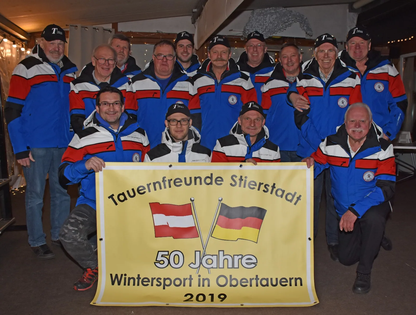 Mitglieder eines Skiclubs in einheitlichen Vereinsjacken mit Jubiläumsbanner