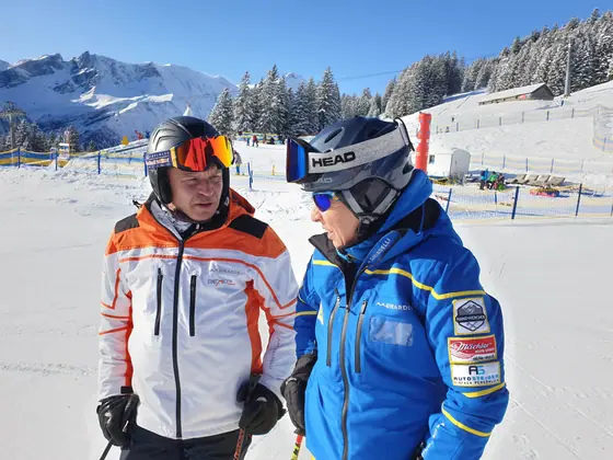 Zwei Skifahrer in Teamjacken mit Helm und Skibrille im Skigebiet
