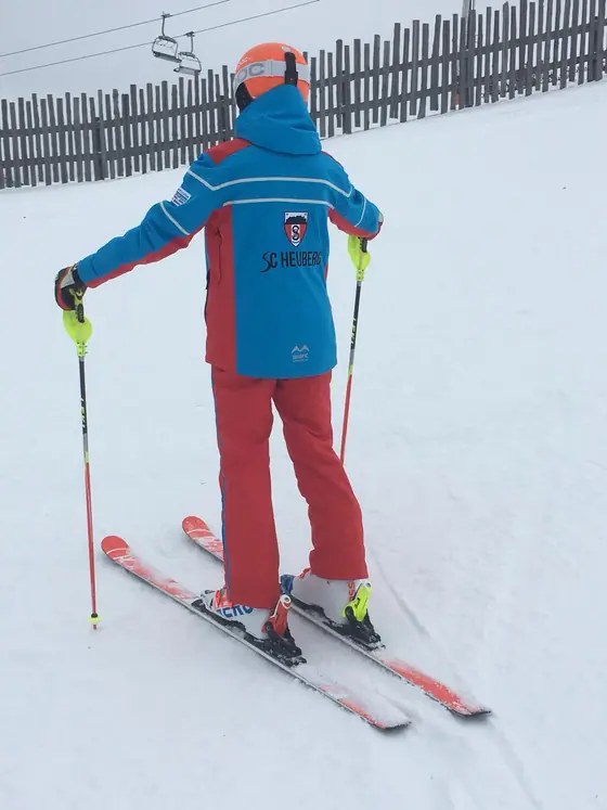 Skilehrer in blauer Teamjacke und roter Skihose auf der Piste