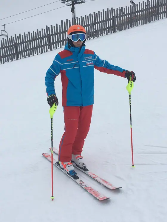 Skilehrer in blau-roter Teambekleidung mit Skistöcken