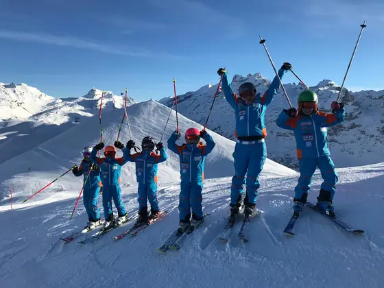 Jubelnde Kinder-Skigruppe in Teambekleidung vor Bergpanorama