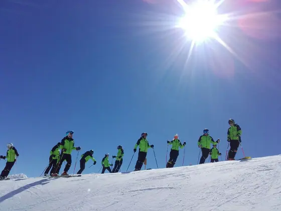 Rennteam in grüner Teambekleidung auf der Piste im Gegenlicht